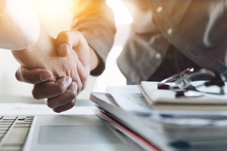 A photo of two people shaking hands over a stack of documents on a desk