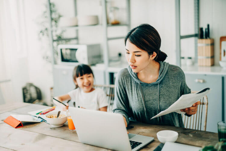 A legal professional on her laptop with her daughter at the dining room table beside her