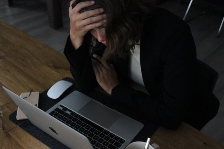 A woman looking stressed as she stares at a laptop likely late at night due to the darkness of the room she's in