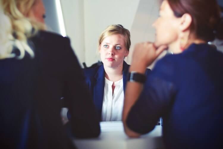 A photo of a young woman looking sad while talking to two other women in a formal work setting