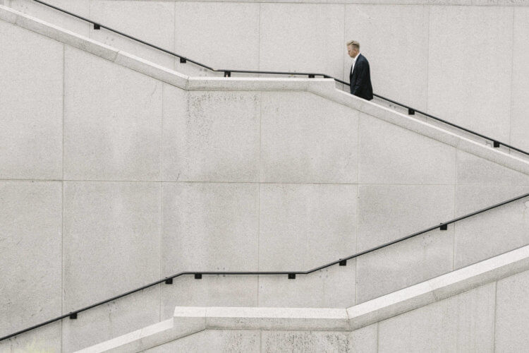 A man in a suit climbs a winding cement staircase.
