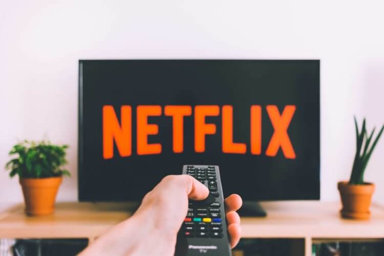 A hand holding a TV remote control pointed at a television with Netflix on it.