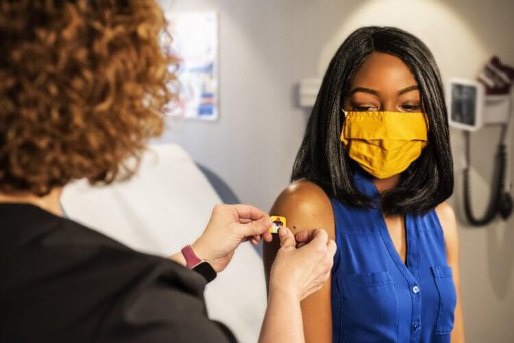 A nurse applies a bandage to a woman's arm, post-vaccination