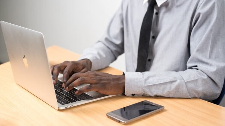 A person typing on a laptop with a phone on the table