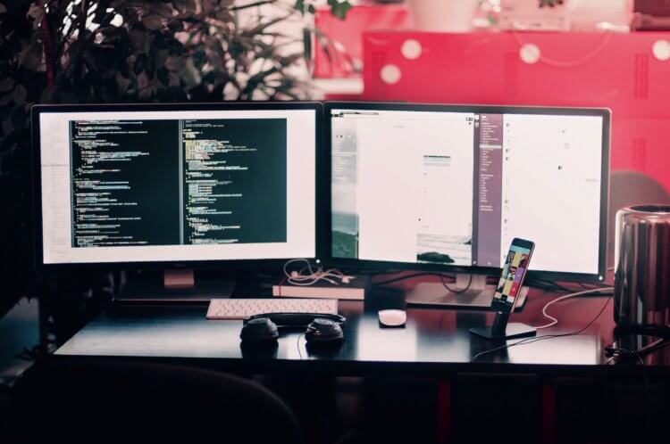 A dual-monitor computer workstation on a desk, with the screens showing snippets of code.