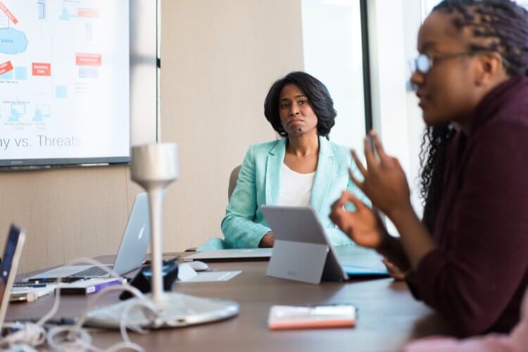 A woman in a business suit listens to another woman, a legal project manager, explain a project