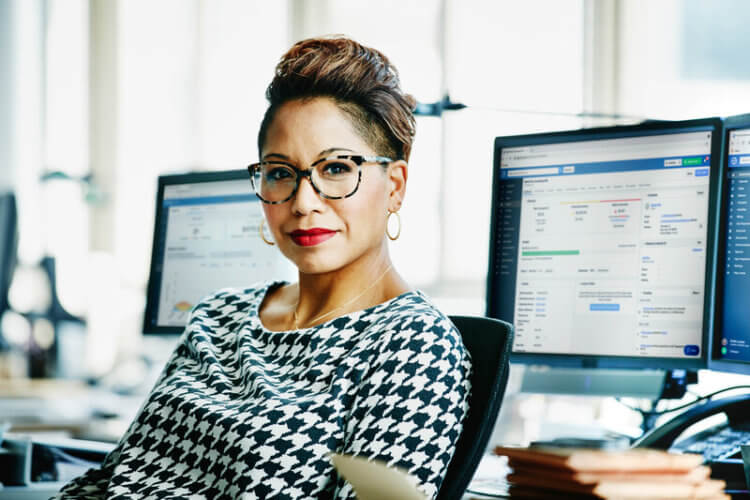 A photo of a legal professional sitting in front of two monitors which display their Clio Manage account