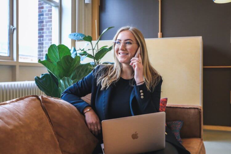 A freelance paralegal sitting on the couch with a laptop while on the phone with one of her clients