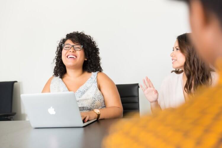 A photo of three paralegals sitting at a table talking while one types on a laptop