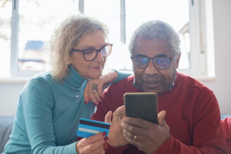 An image of an older couple looking at a smartphone one is holding, the other is holding a credit card