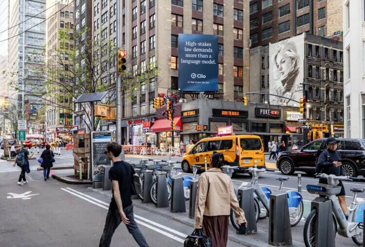 A busy NYC street corner with a digital billboard reading "AI for Fortune 500 legal teams" by Clio above a T-Mobile store.